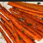 Roasted whole carrots garnished with chopped parsley on a baking sheet.