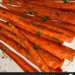 Roasted whole carrots garnished with chopped parsley on a baking sheet.