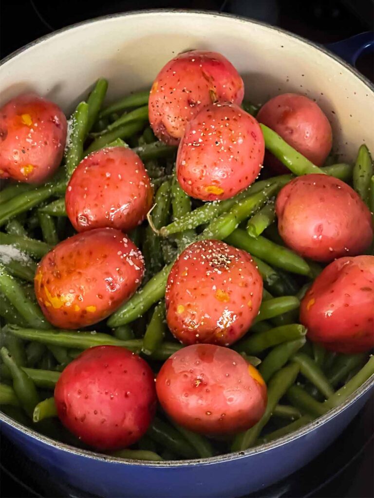 Green beans, baby potatoes, kosher salt and black pepper added to the dutch oven.