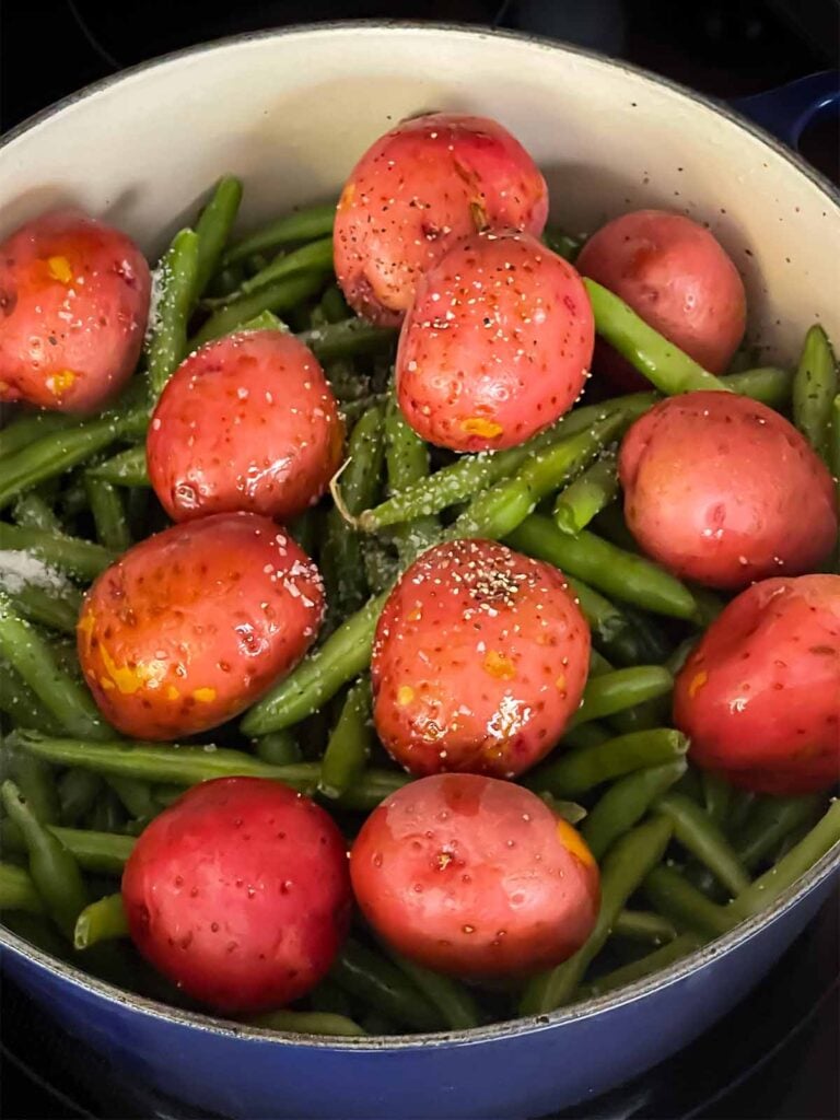 Green beans, baby potatoes, kosher salt and black pepper added to the dutch oven.