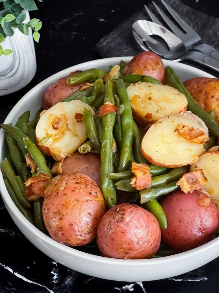 Southern green beans and potatoes in a round light colored bowl on a dark surface.