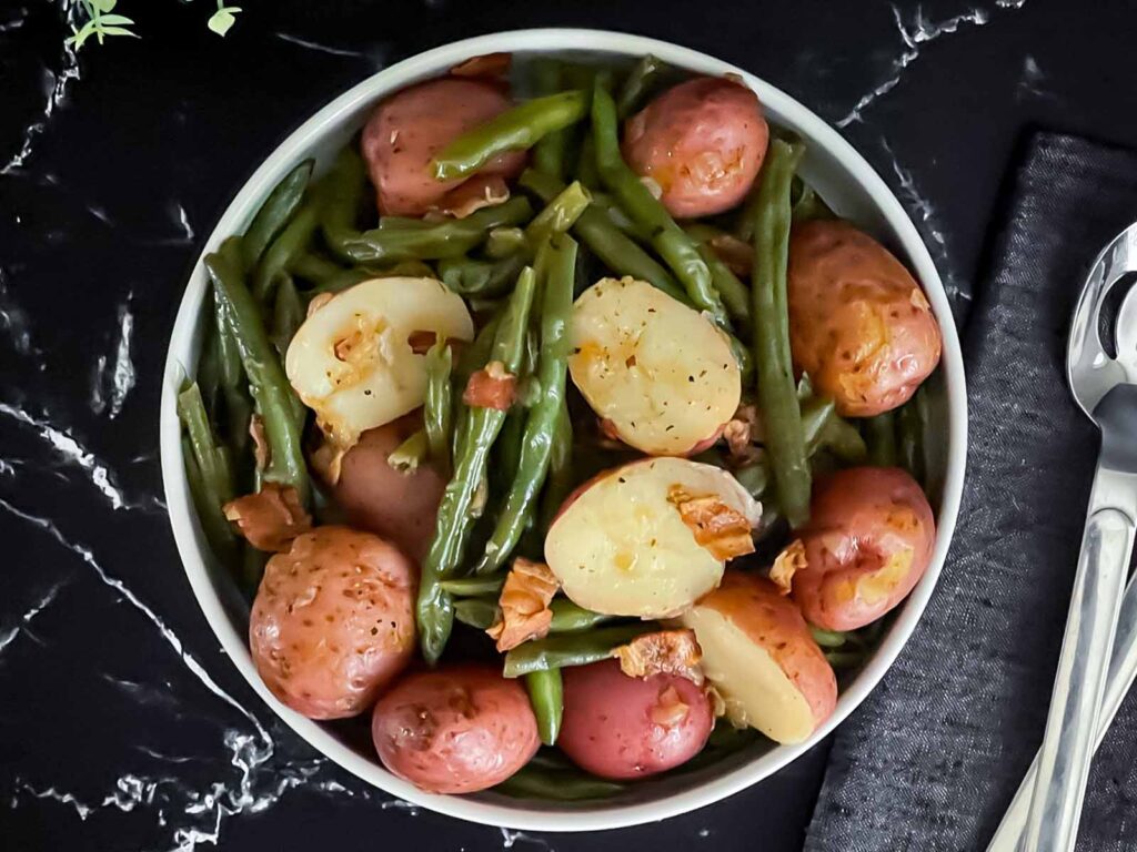 Southern green beans and potatoes in a round light colored bowl on a dark surface.