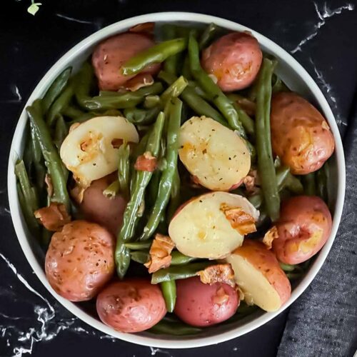 Southern green beans and potatoes in a round light colored bowl on a dark surface.