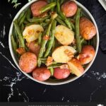 Southern green beans and potatoes in a round light colored bowl on a dark surface.