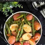 Southern green beans and potatoes in a round light colored bowl on a dark surface.