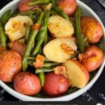 Southern green beans and potatoes in a round light colored bowl on a dark surface.