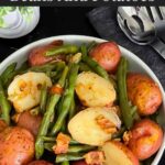 Southern green beans and potatoes in a round light colored bowl on a dark surface.