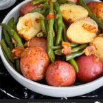 Southern green beans and potatoes in a round light colored bowl on a dark surface.