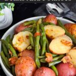 Southern green beans and potatoes in a round light colored bowl on a dark surface.