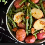 Southern green beans and potatoes in a round light colored bowl on a dark surface.
