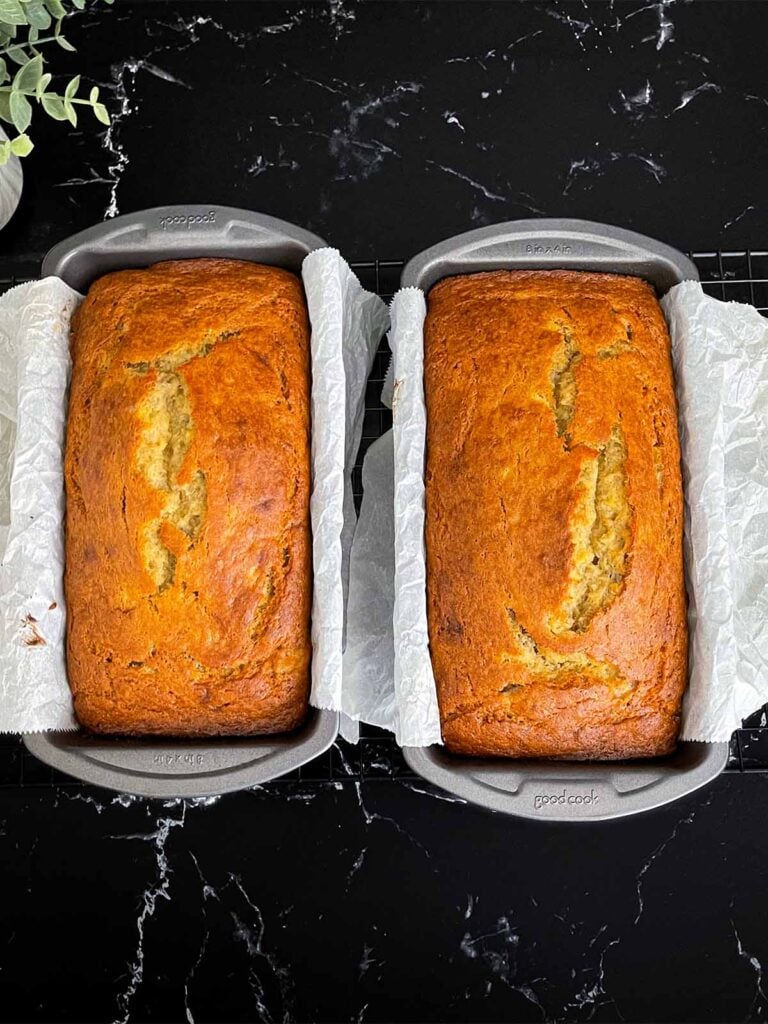 Baked banana bread in two 8x4 loaf pans lined with parchment paper.