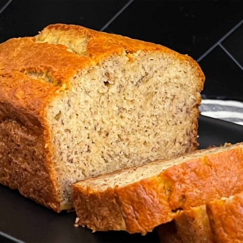 Slices of banana bread and the remaining loaf on a dark plate on a dark surface.