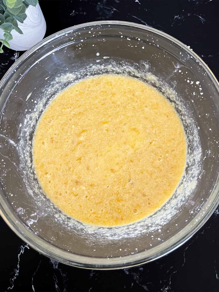 Mashed bananas added to the banana bread batter in a glass mixing bowl.