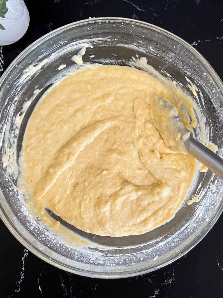 Banana bread batter in a glass mixing bowl on a dark surface.