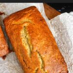 Loaf of banana bread on parchment paper on a wooden board.