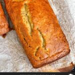 Loaf of banana bread on parchment paper on a wooden board.