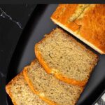 Slices of banana bread and the remaining loaf on a dark plate on a dark surface.