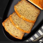 Slices of banana bread and the remaining loaf on a dark plate on a dark surface.