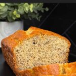 Slices of banana bread and the remaining loaf on a dark plate on a dark surface.