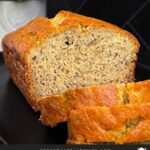 Slices of banana bread and the remaining loaf on a dark plate on a dark surface.