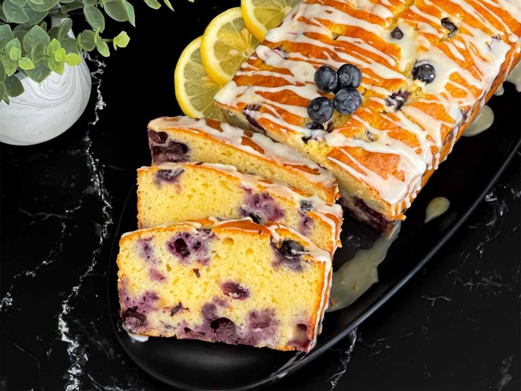 Sliced blueberry bread on a dark platter on a dark surface.