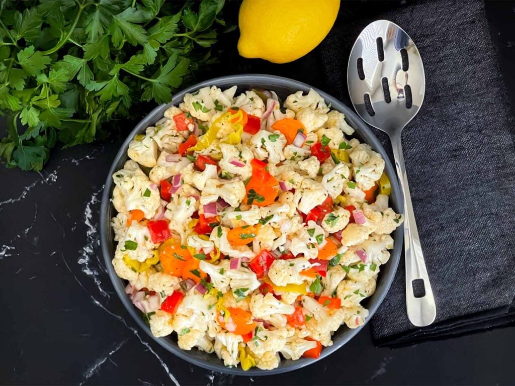 Marinated cauliflower salad in a dark bowl on a dark surface.