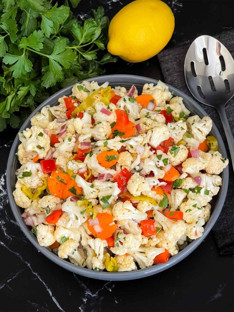 Marinated cauliflower salad in a dark bowl on a dark surface.