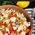 Marinated cauliflower salad in a wooden bowl on a dark surface.