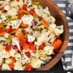 Marinated cauliflower salad in a wooden bowl on a dark surface.