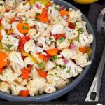 Marinated cauliflower salad in a dark bowl on a dark surface.