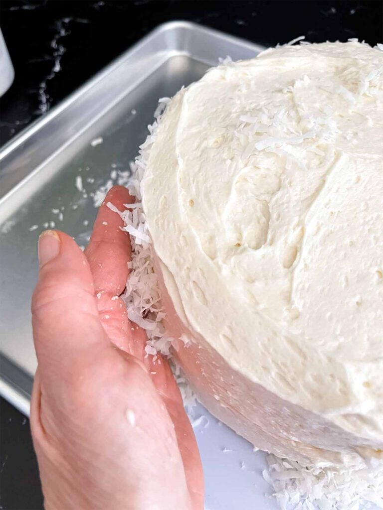 A hand full of shredded coconut placing it on the sides of the coconut cake.