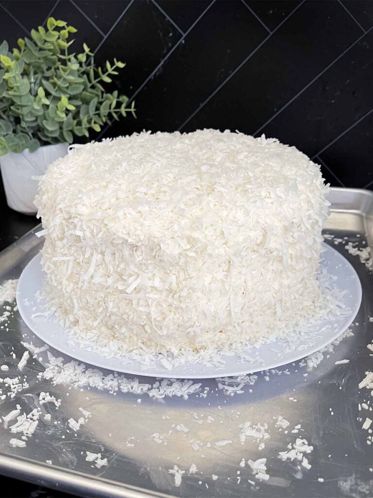 Frosted coconut cake with the shredded coconut pressed into the icing on a light plate on a baking sheet.