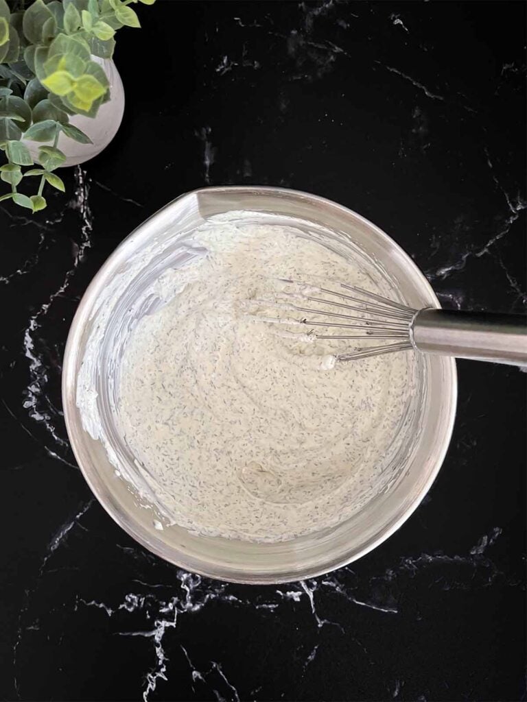 Dill dip whisked together in a metal bowl on a dark surface.