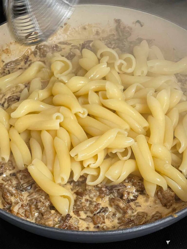 Adding pasta to a Pasta alla Norcina sauce in a skillet.