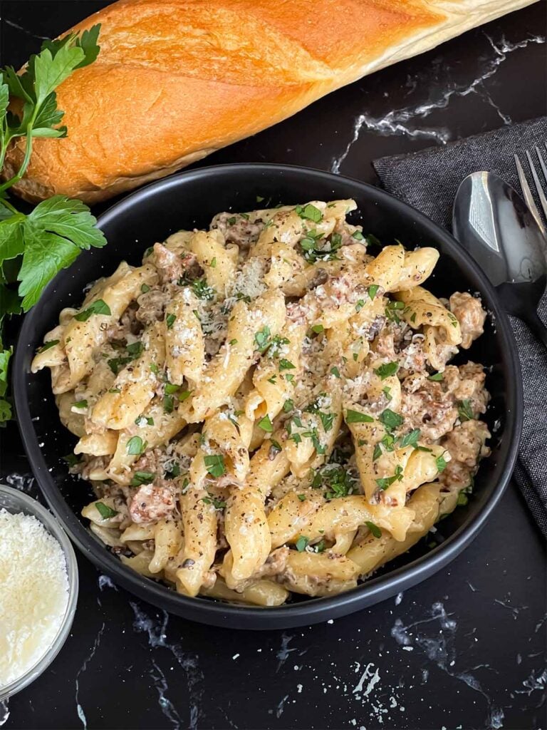 Pasta alla Norcina in a dark bowl with bread and parsley in the background.