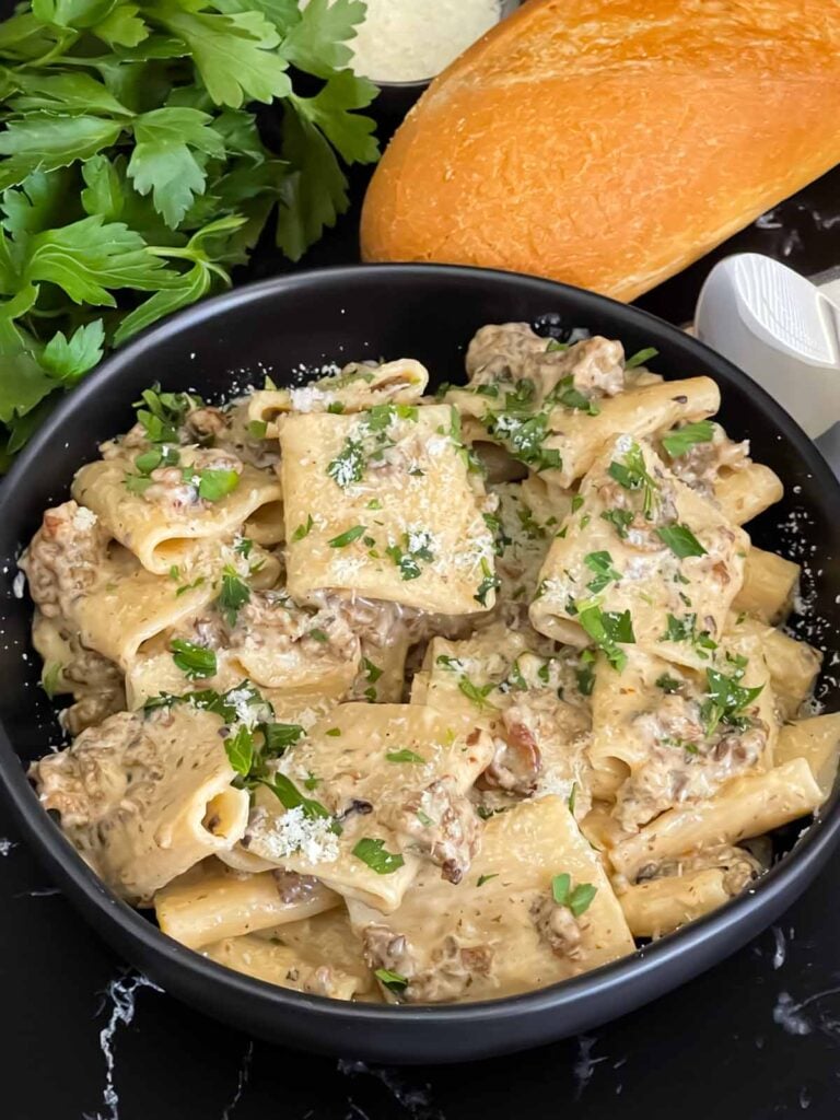 Pasta alla Norcina in a dark bowl with bread and parsley in the background.