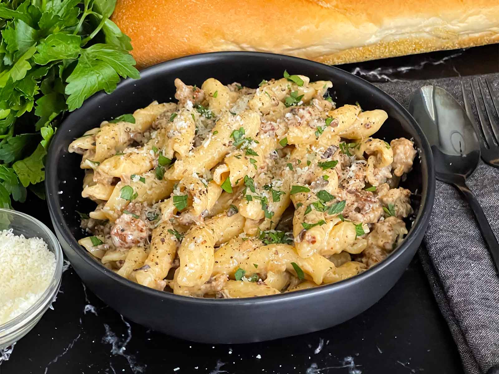 A bowl of pasta alla norcina garnished with chopped parsley on a dark surface.