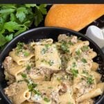 Pasta alla Norcina in a dark bowl with bread and parsley in the background.