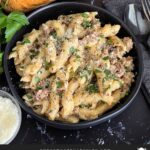 Pasta alla Norcina in a dark bowl with bread and parsley in the background.