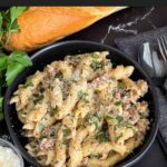 Pasta alla Norcina in a dark bowl with bread and parsley in the background.