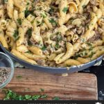 Pasta alla Norcina in a dark bowl with bread and parsley in the background.