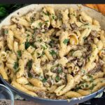 Pasta alla Norcina in a dark bowl with bread and parsley in the background.