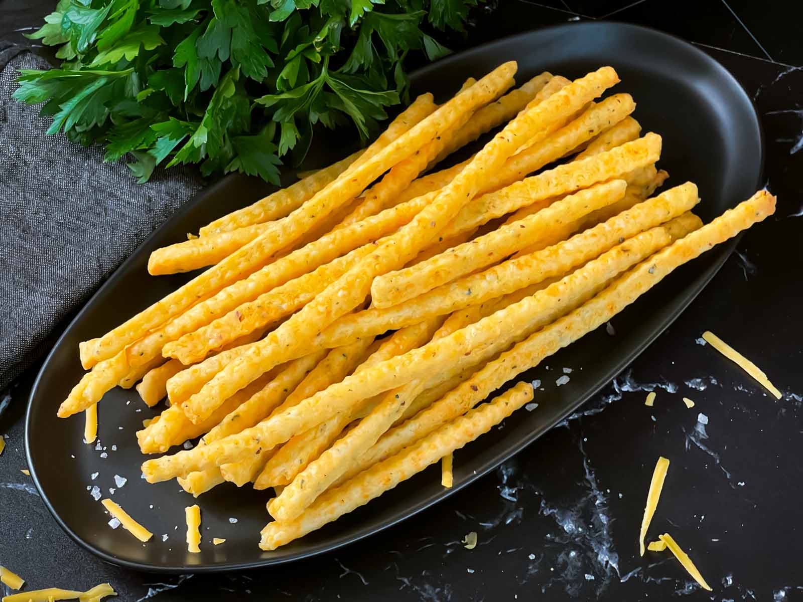 Cheddar cheese and herb straws on a oval dark platter.
