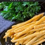 Cheddar and herb cheese straws on a black plate.