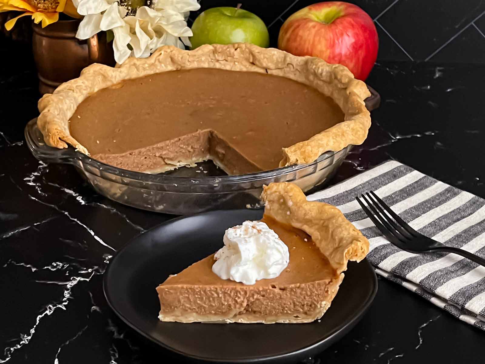 A slice of apple butter pie garnished with whipped cream on a round dark plate.