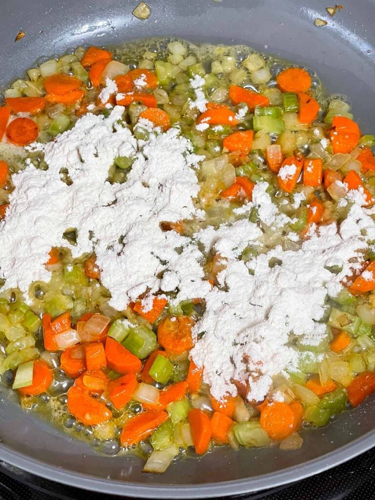 Flour being added to a mirepoix in a skillet.