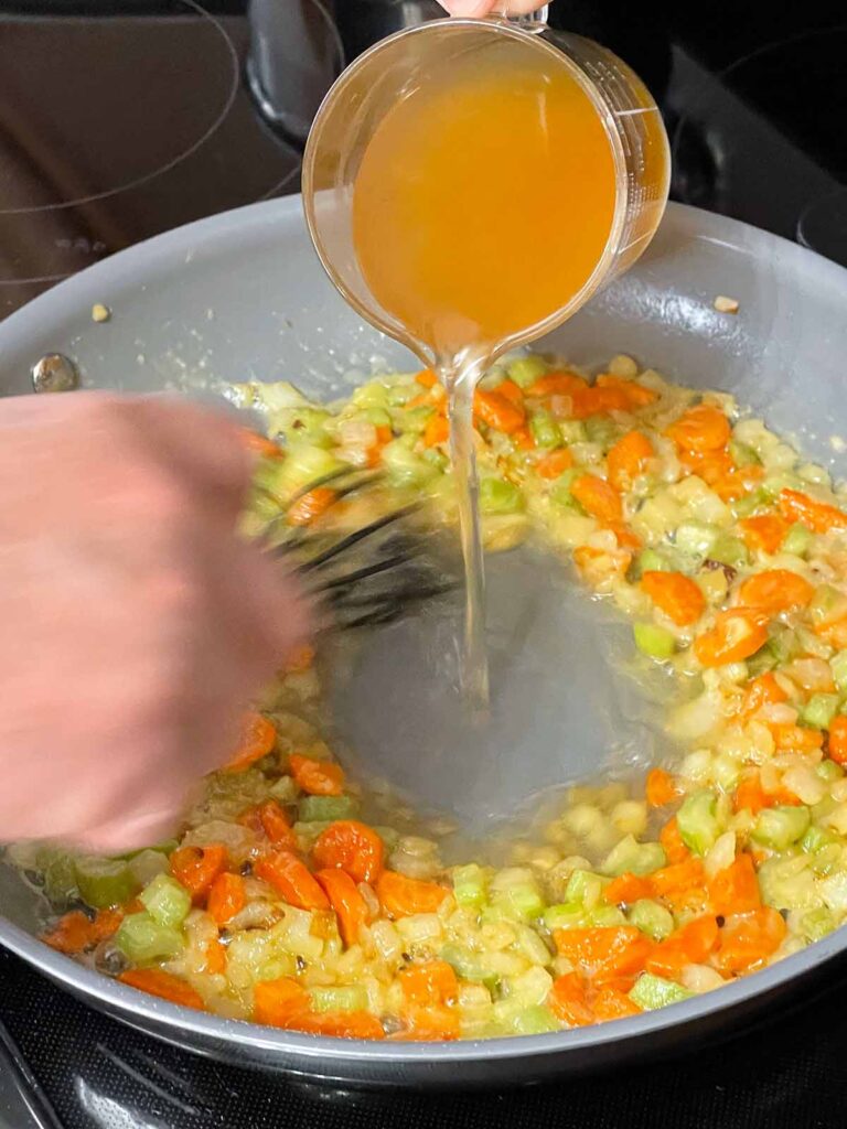 Adding chicken stock to mirepoix and roux.