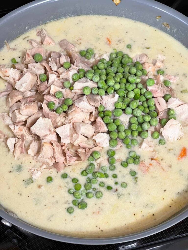 Adding the chicken and peas to the sauce for chicken stuffing casserole.