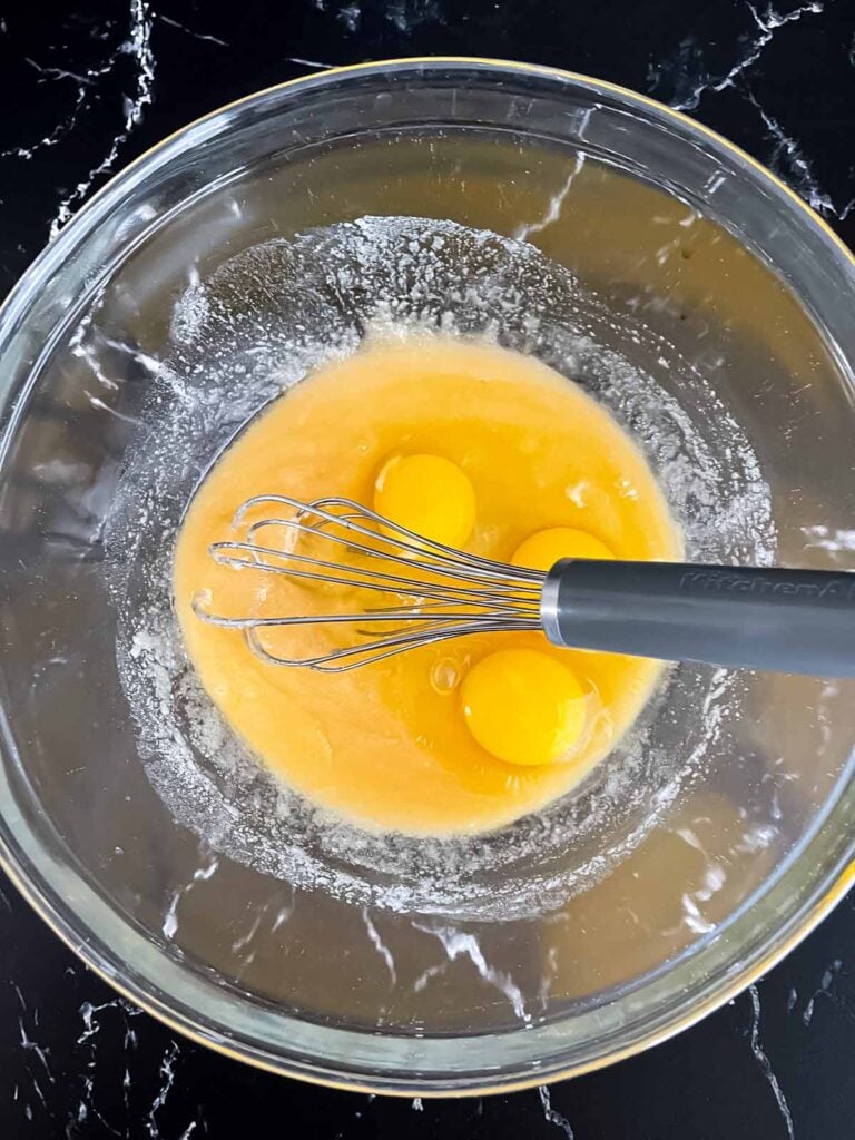 Eggs added to a sugar butter mixture in a glass bowl.