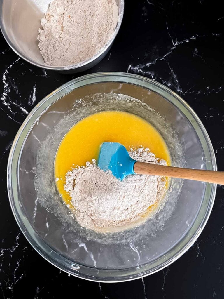 Flour added to a butter egg mixture in a glass bowl.